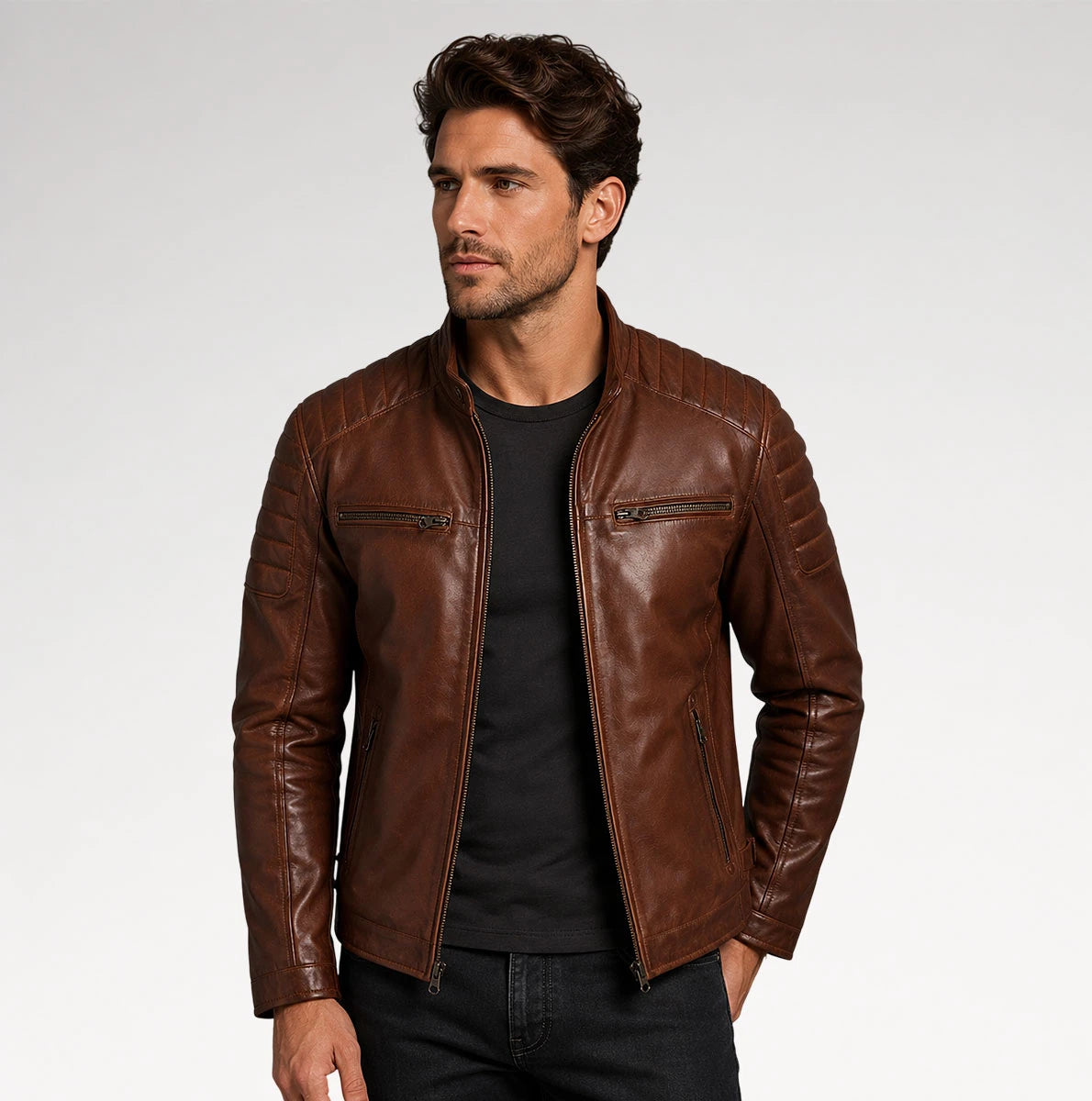 A man wearing a brown leather moto jacket over a black t-shirt and dark jeans, photographed against a light gray studio background. Main image