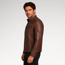 A man wearing a brown leather jacket, shown in profile against a light gray studio background.