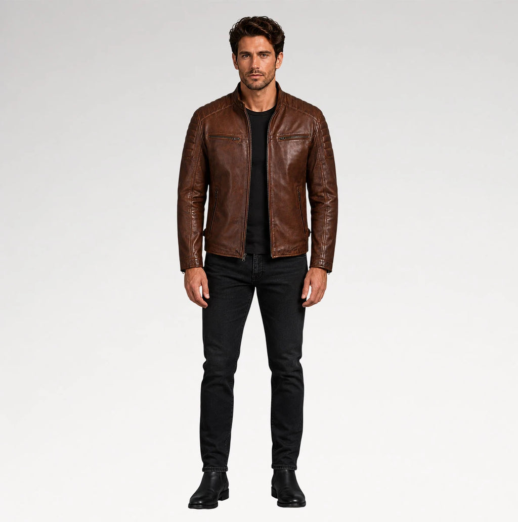 A man modeling a brown leather jacket, black t-shirt, black jeans, and black boots against a light gray studio background.