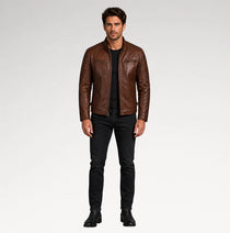 A man modeling a brown leather jacket, black t-shirt, black jeans, and black boots against a light gray studio background.