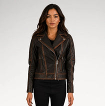A woman modeling a dark brown distressed leather moto jacket with silver zippers and contrast stitching, paired with black pants against a light gray studio background.