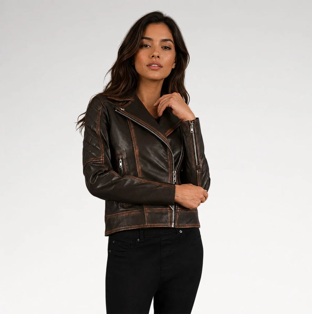 A woman modeling a dark brown distressed leather moto jacket with silver zippers, paired with black pants, against a light gray studio background.