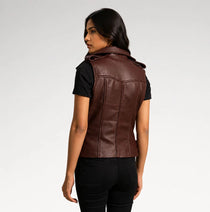 A woman shown from the back wearing a dark brown leather sleeveless vest over a black t-shirt and black jeans, photographed against a light gray studio background.