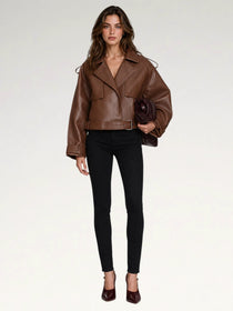 A woman modeling a brown leather moto jacket with a belted waist, paired with black skinny pants and burgundy heels, holding a dark brown clutch against a plain white studio background.