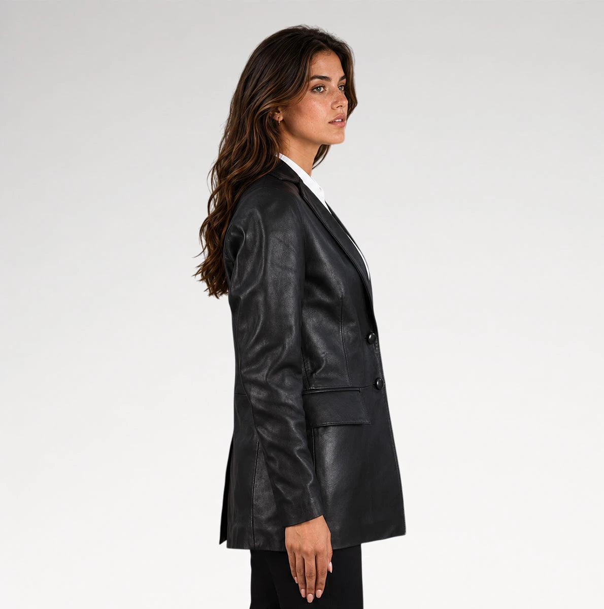 A woman in side profile wearing a black leather blazer over a white collared shirt, photographed against a clean light gray studio background.