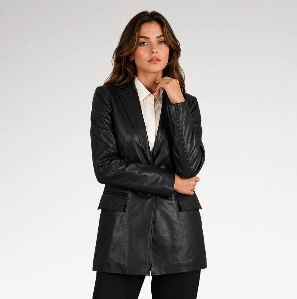 A woman modeling a black faux-leather blazer with a structured silhouette, worn over a white collared shirt, against a plain light gray studio background.