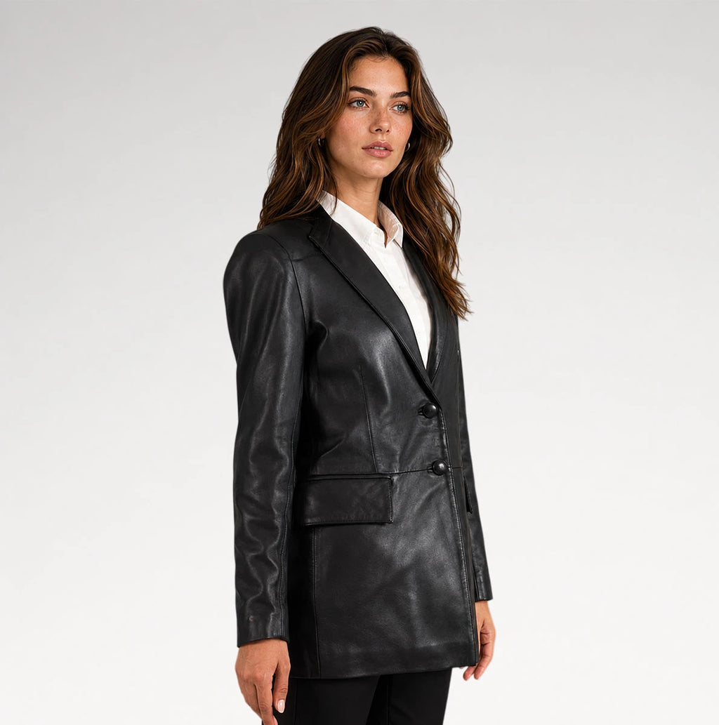 A woman modeling a black faux-leather blazer with a white collared shirt underneath, photographed against a plain light gray studio background.