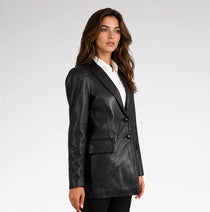 A woman modeling a black faux-leather blazer with a white collared shirt underneath, photographed against a plain light gray studio background.