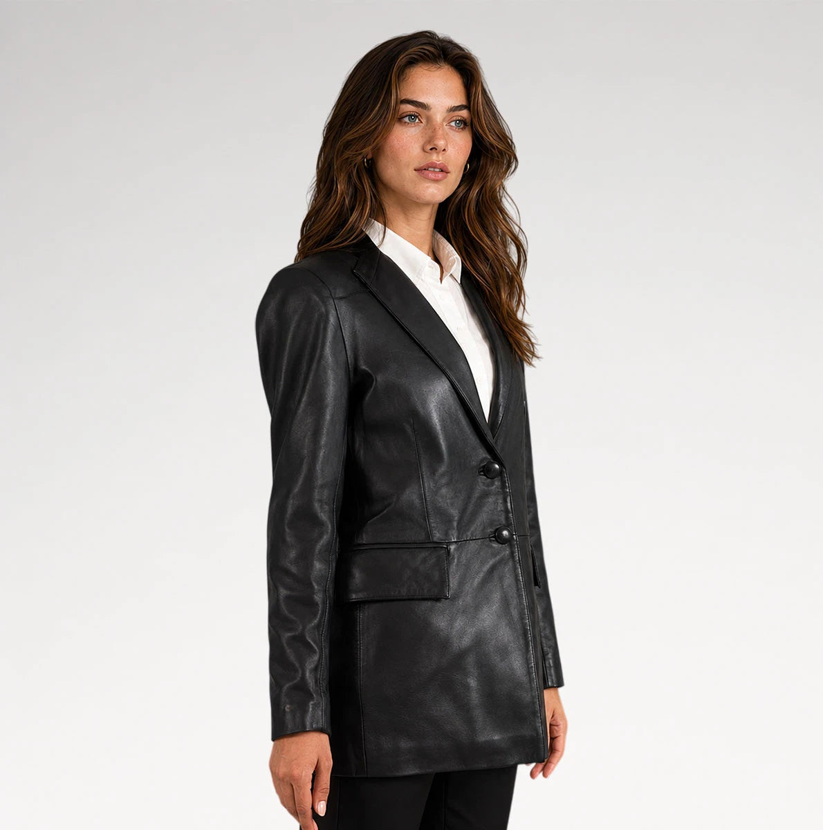 A woman modeling a black faux-leather blazer with a white collared shirt underneath, photographed against a plain light gray studio background.