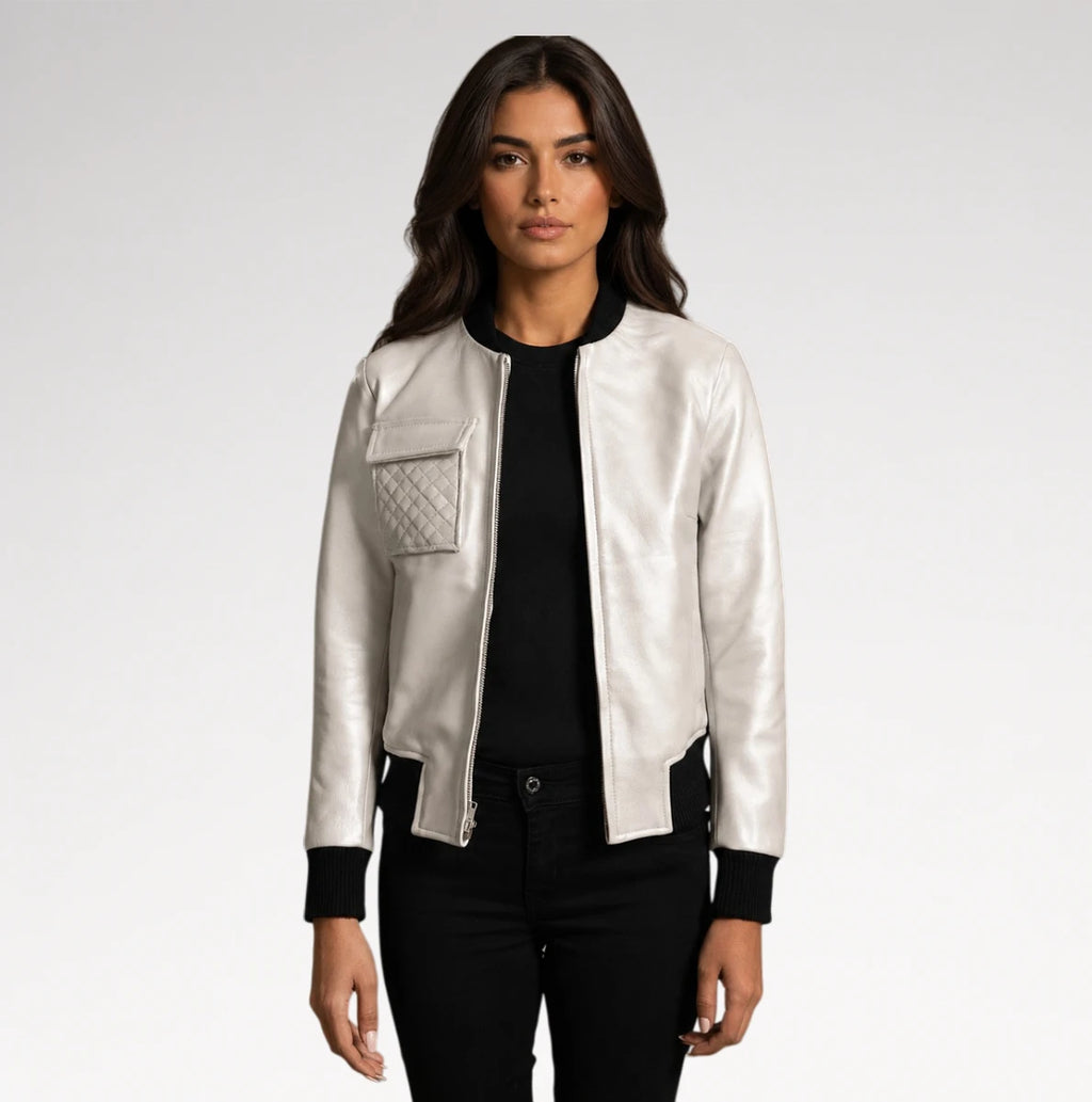 A woman modeling a shiny silver bomber jacket with black ribbed trim, a black top, and black pants against a light gray studio background.