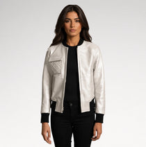 A woman modeling a shiny silver bomber jacket with black ribbed trim, a black top, and black pants against a light gray studio background.