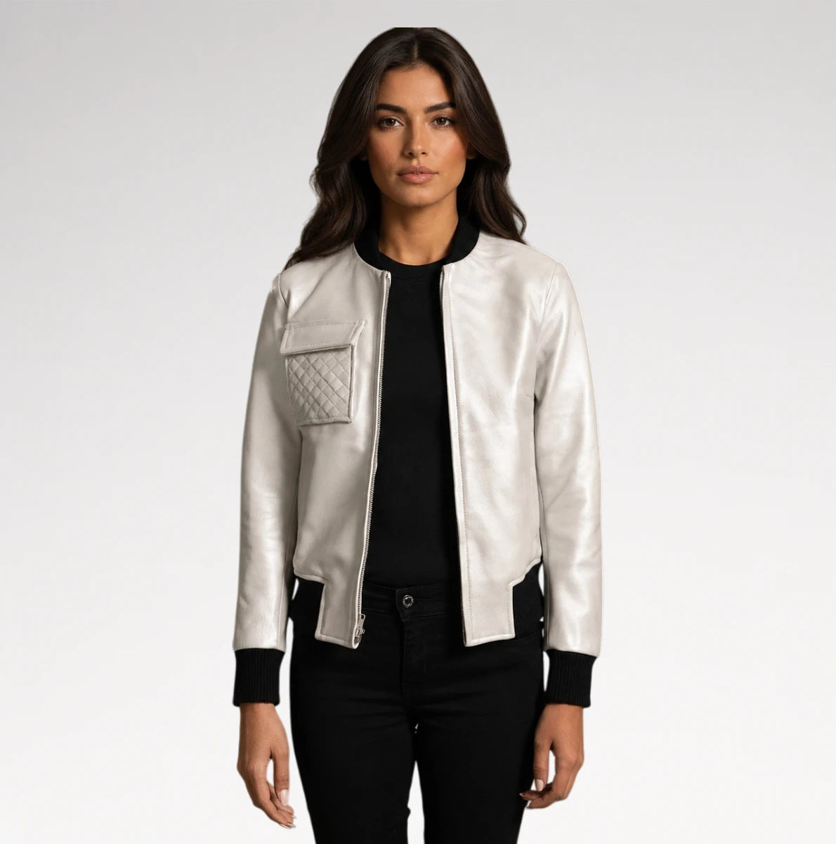 A woman modeling a shiny silver bomber jacket with black ribbed trim, a black top, and black pants against a light gray studio background.
