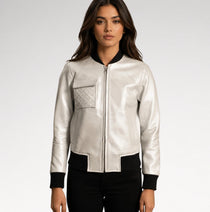 A woman modeling a shiny silver faux-leather bomber jacket with black ribbed trim on the collar, cuffs, and hem, paired with black pants against a light gray studio background.