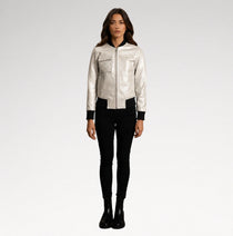 A woman modeling a shiny silver bomber jacket with black trim, paired with black skinny pants and black boots, against a light gray studio background.
