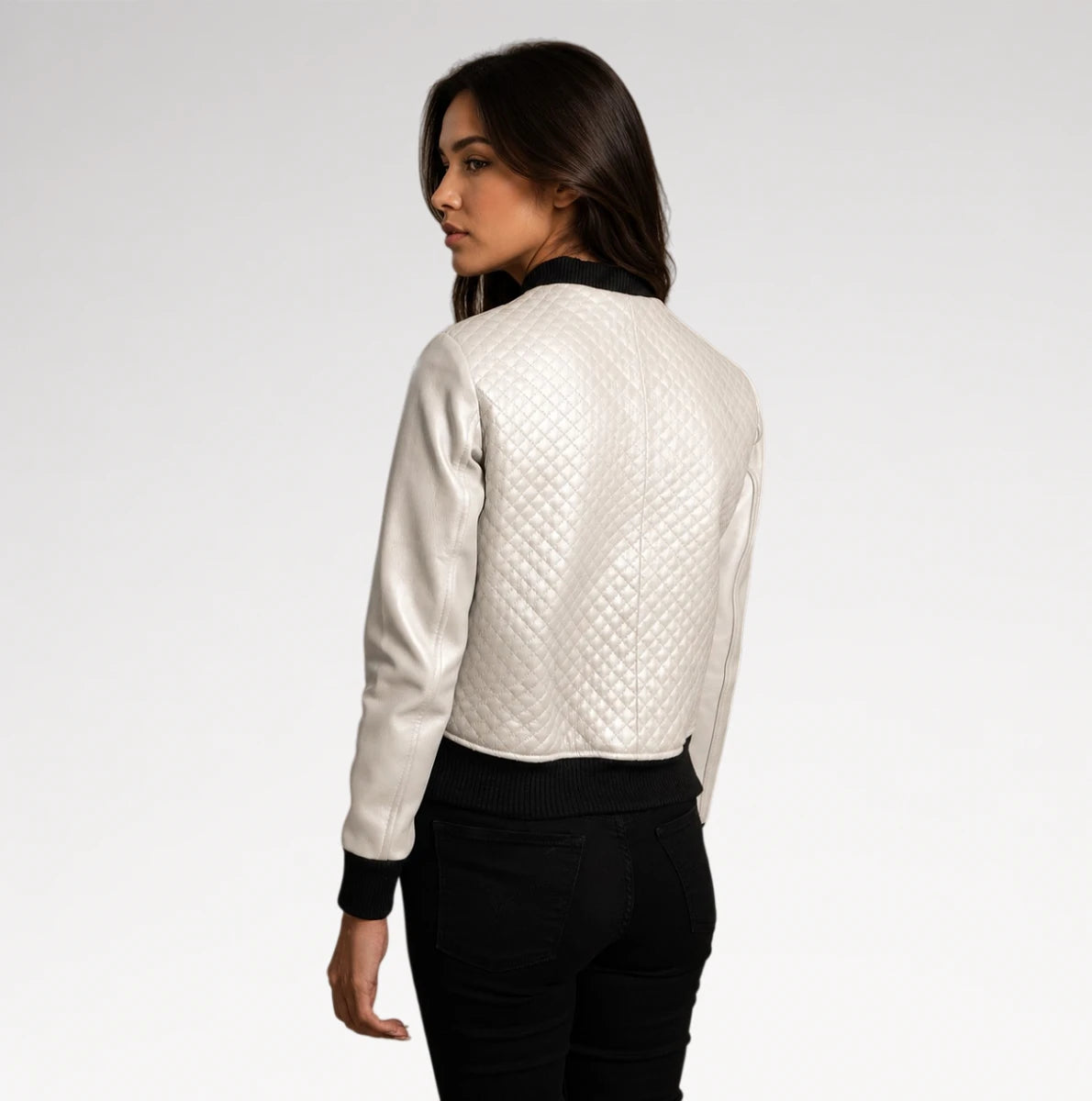 A woman shown from the back wearing a white quilted bomber jacket with black ribbed cuffs and collar, paired with black pants, against a light gray studio background.