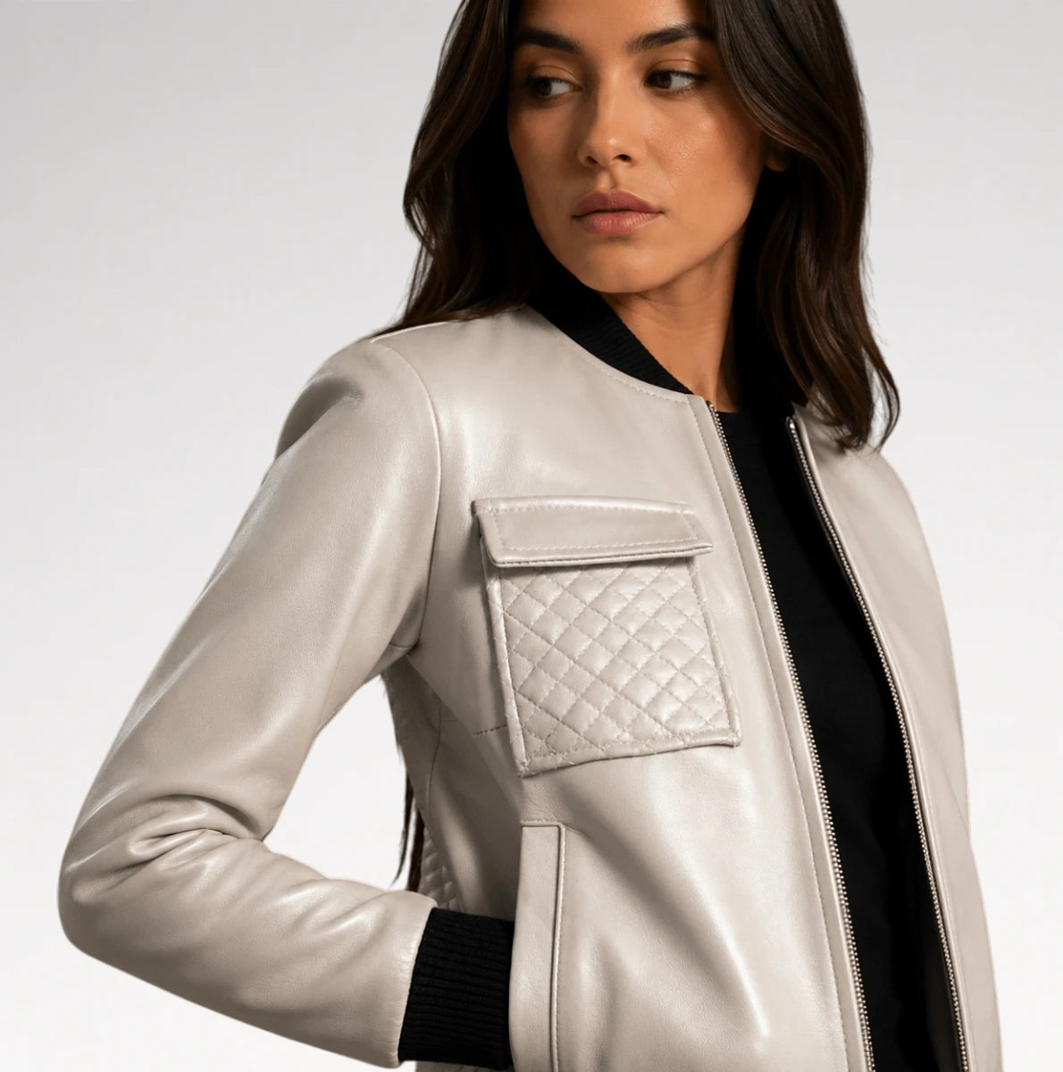 A woman wearing a light silver faux leather bomber jacket with a quilted chest pocket and black ribbed trim, photographed against a light gray studio background.