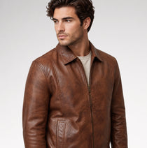 A man wearing a brown leather jacket over a light beige t-shirt, photographed against a neutral light gray background.