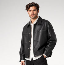 A man wearing a black leather jacket over a white button-up shirt, photographed against a clean light gray studio background.