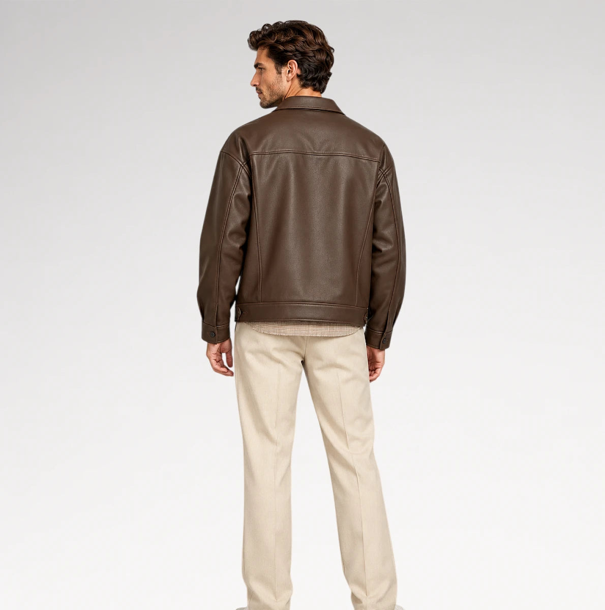 A man shown from the back wearing a dark brown leather jacket and beige trousers, standing against a light gray studio background.