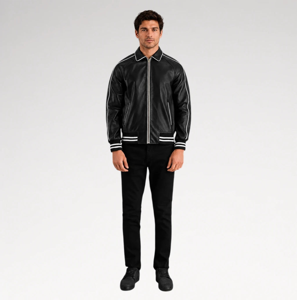 A man modeling a black leather bomber jacket with white contrast stitching and striped ribbed collar, cuffs, and hem, paired with black pants and black shoes, against a light gray studio background.