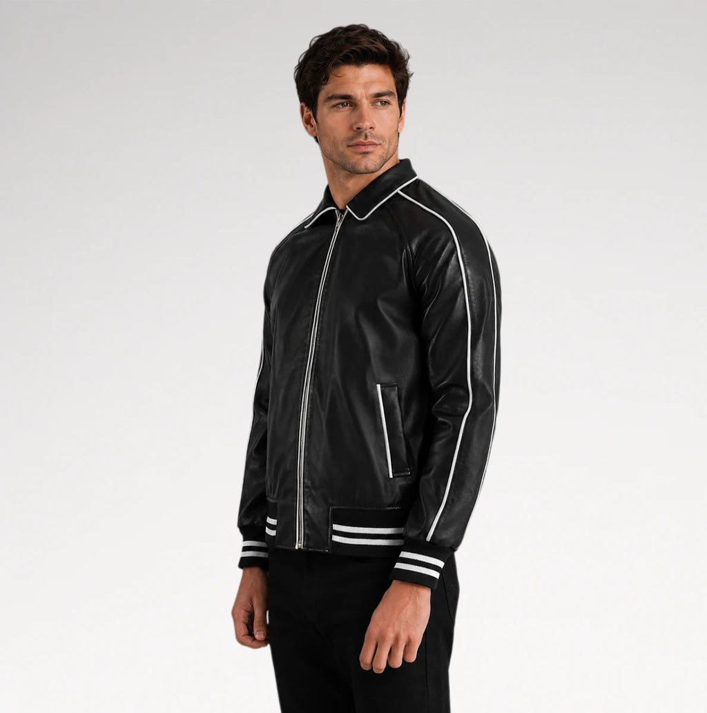 A man wearing a black leather bomber jacket with white contrast stitching and striped ribbed cuffs, standing against a light gray studio background.