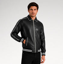 A man wearing a black leather bomber jacket with white contrast piping and striped ribbed cuffs and hem, posed against a light gray studio background.