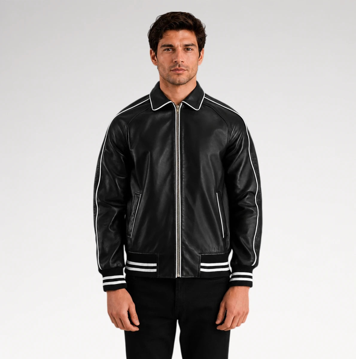 A man wearing a black leather bomber jacket with white contrast piping, a white collar, and white stripes on the cuffs and hem, paired with black pants against a light gray studio background.