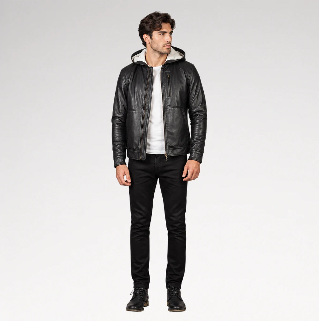 A man modeling a black leather hooded jacket with a light-colored lining, worn over a white t-shirt and black jeans, against a plain light gray studio background.