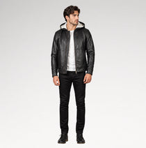 A man modeling a black leather hooded jacket with a light-colored lining, worn over a white t-shirt and black jeans, against a plain light gray studio background.