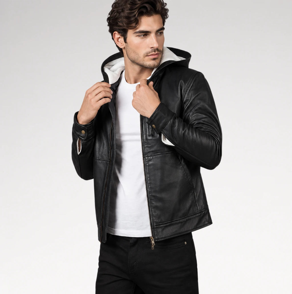 A man wearing a black faux-leather hooded jacket with a white hood lining, styled over a white t-shirt and black jeans, photographed against a light gray studio background.