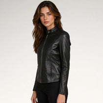 A woman modeling a black leather jacket with a high collar and front zipper, paired with black pants, against a plain light gray studio background.