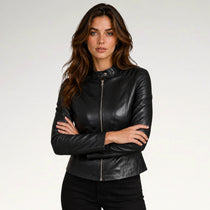 A woman modeling a black faux-leather moto jacket with a front zipper, set against a plain light gray studio background.