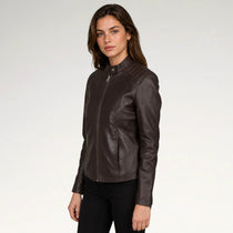 A woman modeling a dark brown leather jacket with a mock neck and front zipper, paired with black pants, against a plain light gray studio background.
