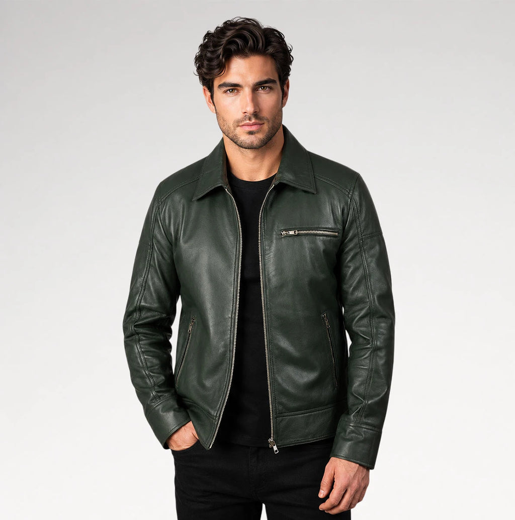 A man wearing a dark green leather jacket over a black t-shirt and black pants, standing against a light gray studio background.