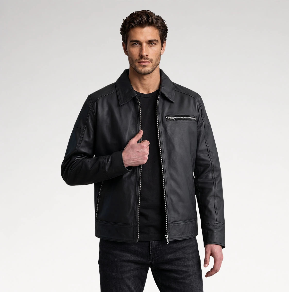 A man wearing a black leather motorcycle jacket with a zippered chest pocket, styled over a black t-shirt and dark jeans, photographed against a light gray studio background. Main image