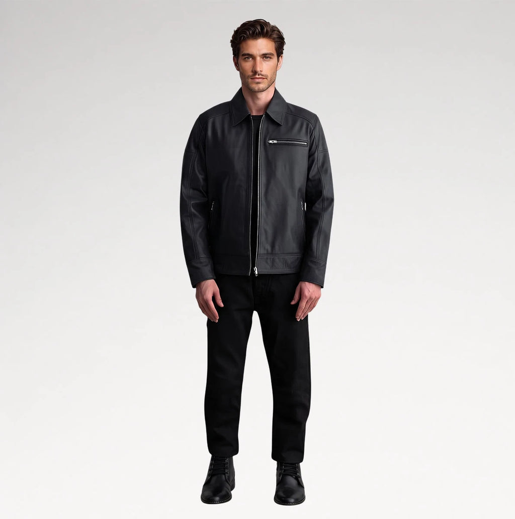 A man modeling a black leather jacket with a zippered chest pocket, paired with black trousers and black shoes, against a light gray studio background.
