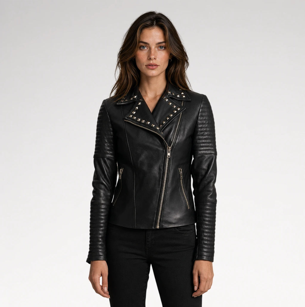 A woman modeling a black leather moto jacket with silver studs and zippers, paired with black pants, against a light gray studio background.