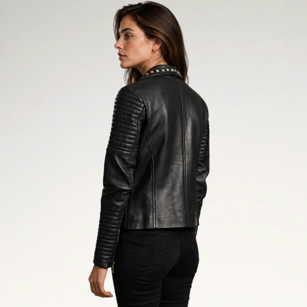A woman shown from the back wearing a black leather jacket with quilted sleeves and studded collar details, paired with black pants, against a plain light gray studio background.
