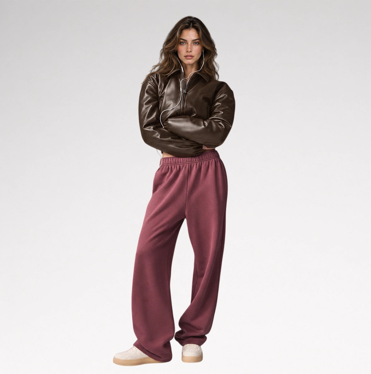 A model stands against a light gray studio background wearing a dark brown faux-leather cropped jacket and dusty rose wide-leg sweatpants.