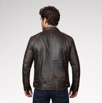 A man viewed from the back wearing a dark brown leather jacket with contrasting tan stitching, paired with dark blue jeans, against a light gray studio background.