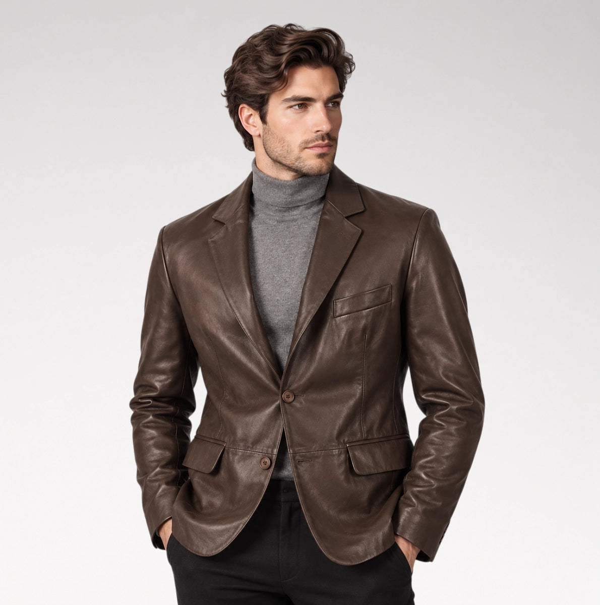 A man wearing a dark brown leather blazer over a gray turtleneck sweater and black pants, standing against a light gray studio background.