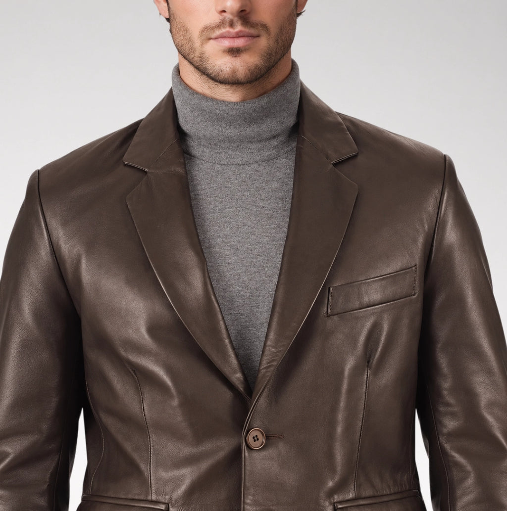 A man wearing a dark brown leather blazer over a gray turtleneck sweater, shown from the chin down against a light gray studio background.