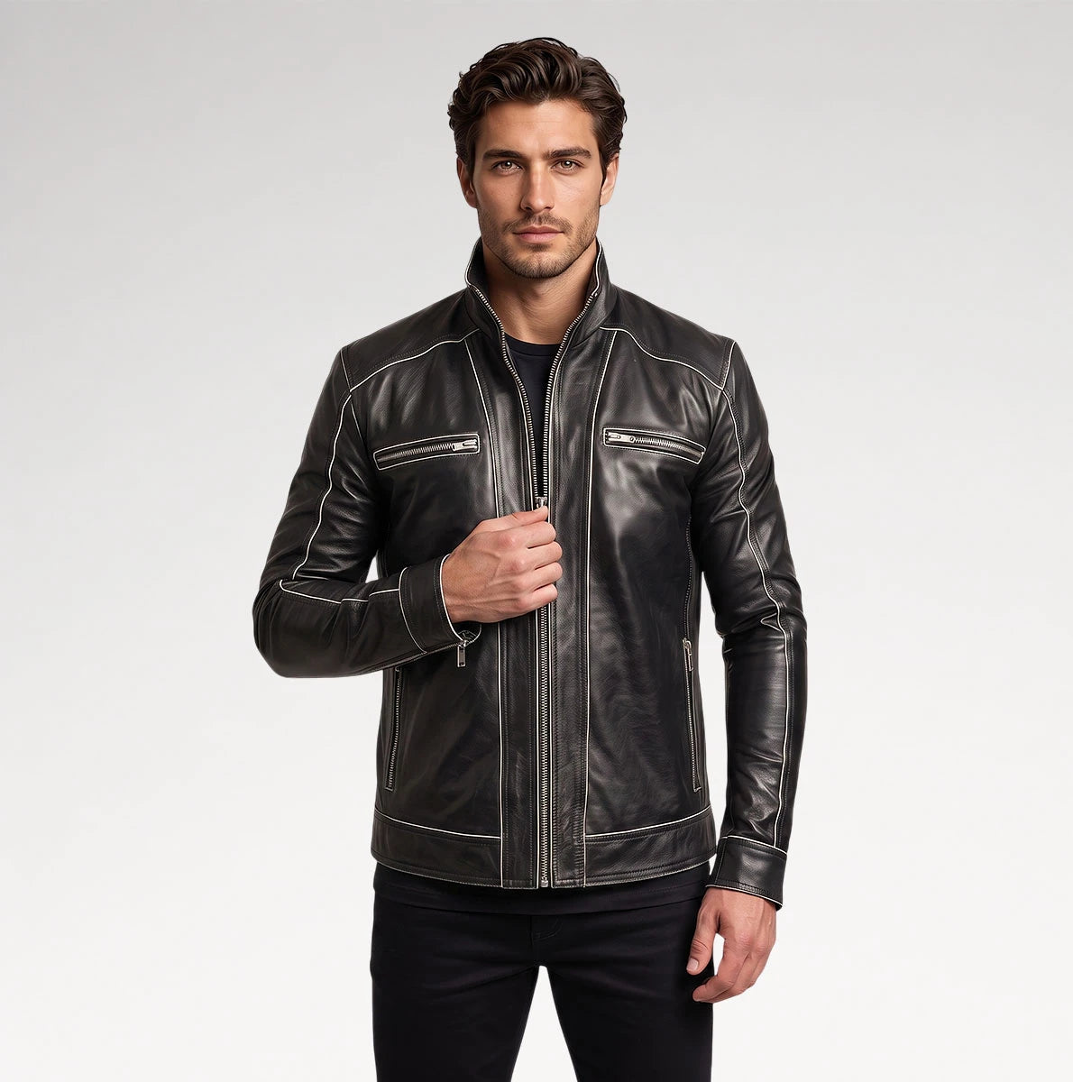 A man wearing a black leather motorcycle jacket with white contrast stitching and silver zippers, paired with black pants, against a light gray studio background.