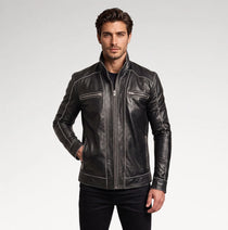 A man wearing a black leather motorcycle jacket with white contrast stitching and silver zippers, paired with black pants, against a light gray studio background.