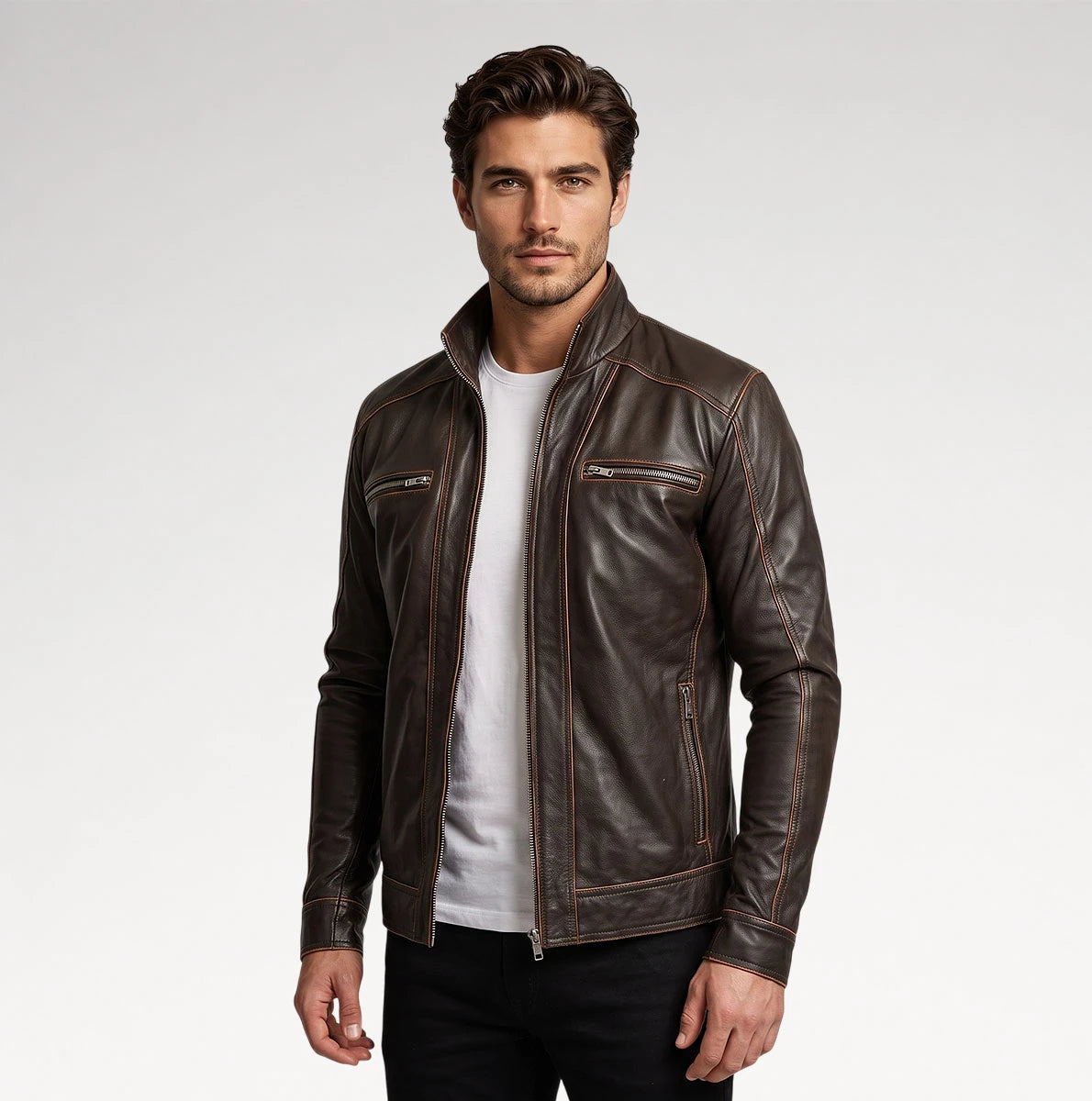 A man wearing a dark brown leather motorcycle jacket over a white t-shirt and black pants, standing against a light gray studio background. Main image