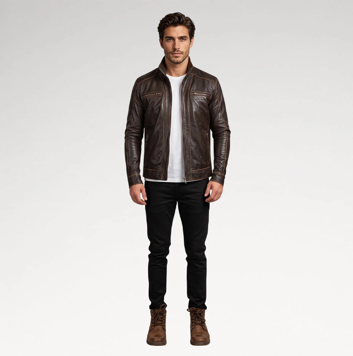 A man modeling a dark brown leather jacket over a white t-shirt, black jeans, and brown boots, standing against a light gray studio background.