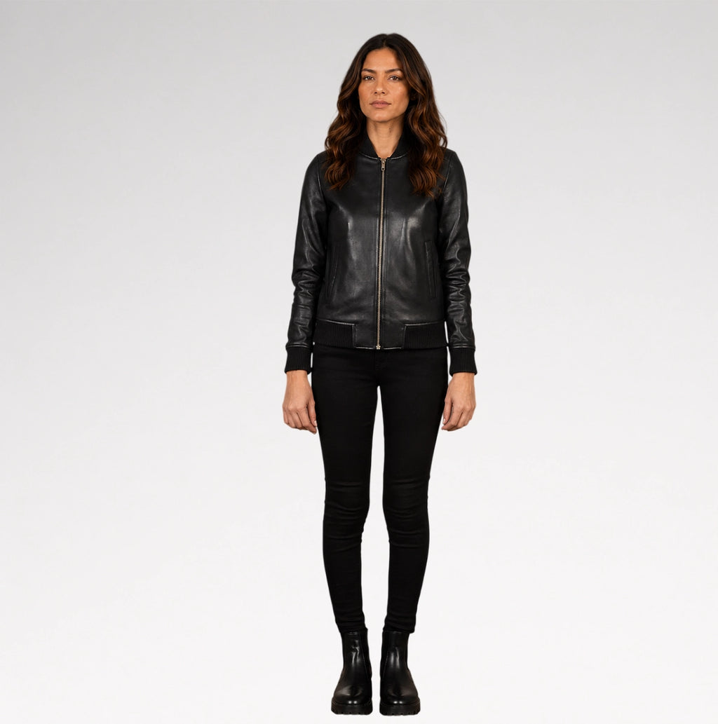 A woman modeling a black leather bomber jacket with a front zipper, paired with black skinny pants and black ankle boots, against a light gray studio background.