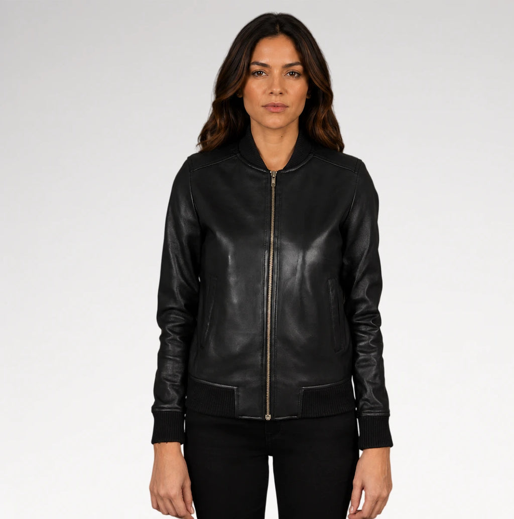 A woman modeling a black leather bomber jacket with a front zipper, ribbed collar, cuffs, and hem, paired with black pants against a light gray studio background.
