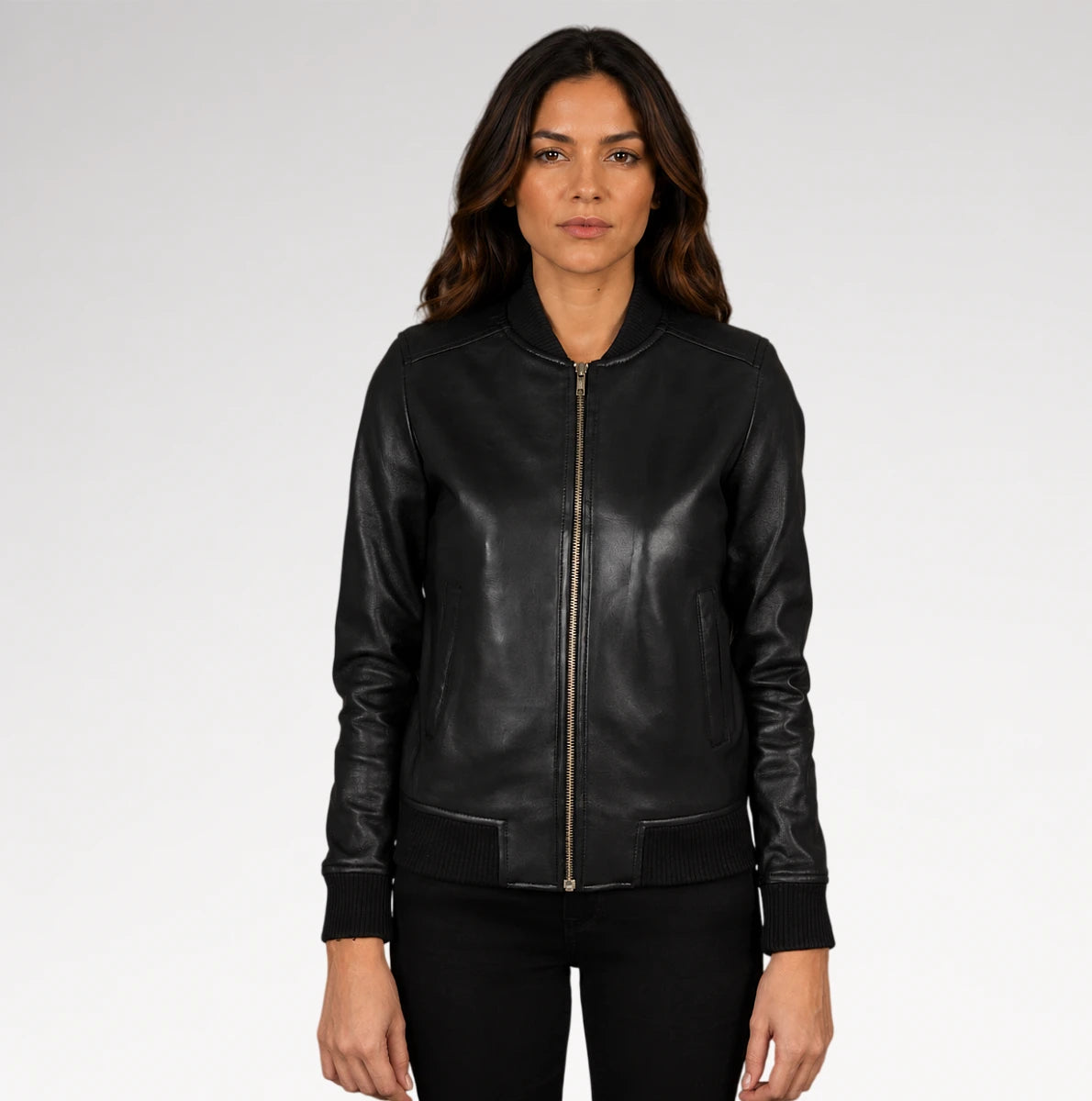A woman modeling a black leather bomber jacket with a front zipper, ribbed collar, cuffs, and hem, paired with black pants against a light gray studio background.