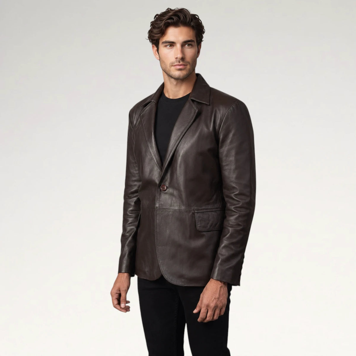 A man wearing a dark brown leather blazer over a black t-shirt and black pants, standing against a light gray studio background. Main image